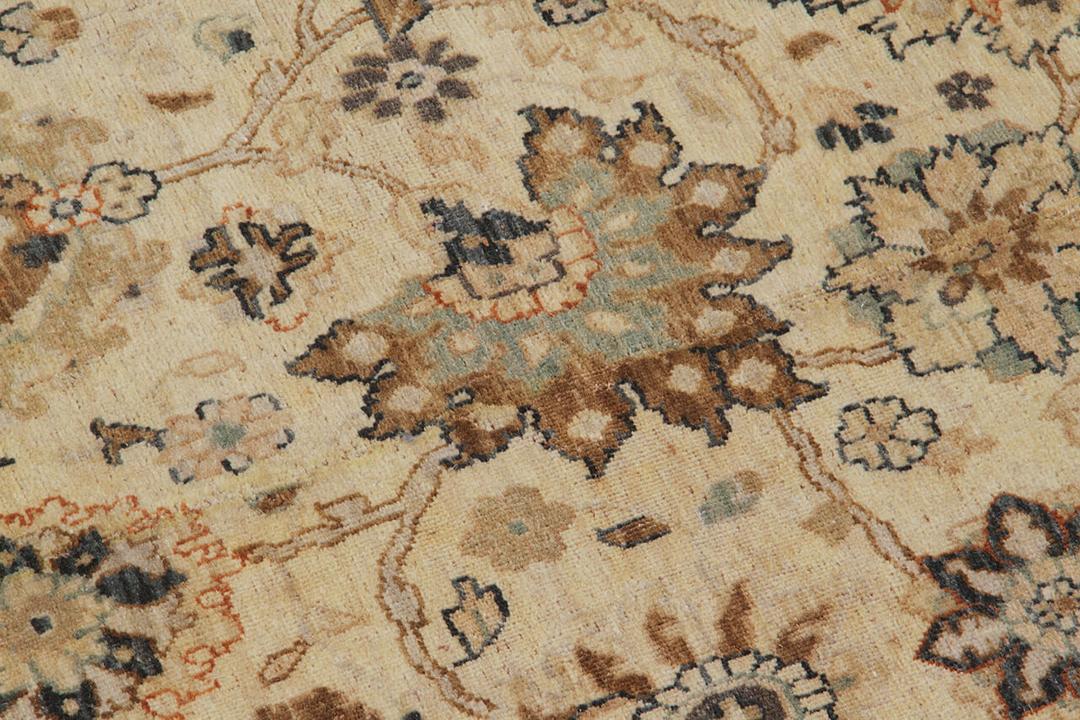 Een handgeknoopt beige tapijt uit India met een verfijnd medaillonpatroon van bloemen.