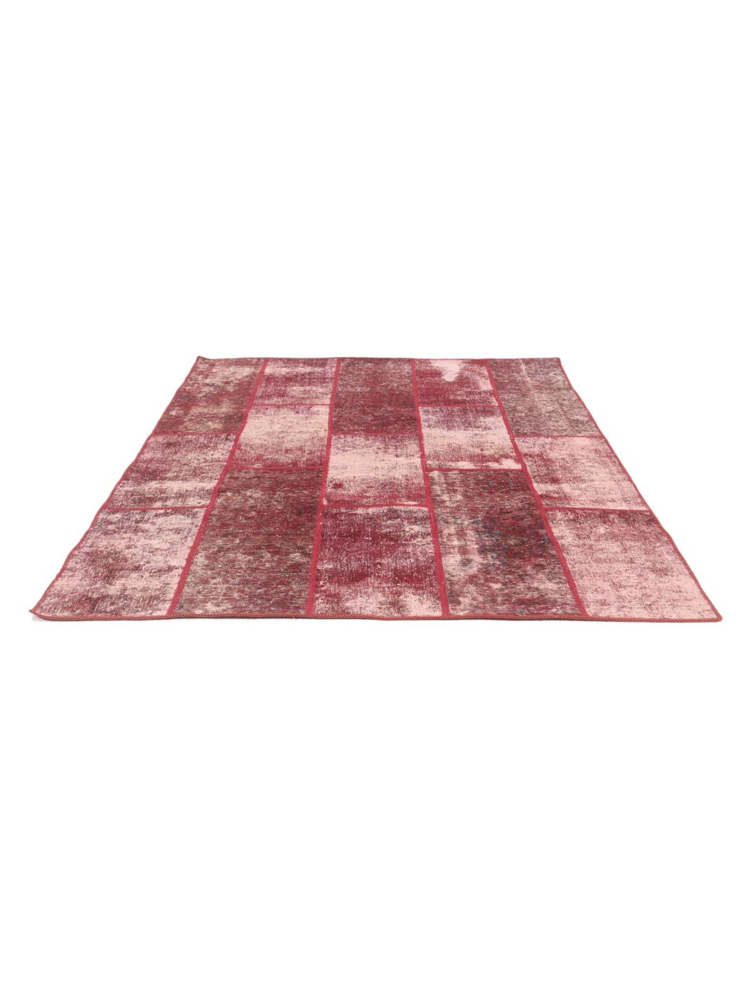 A rectangular patchwork rug with various shades of dark-red and pink tones in a hand-knotted design.