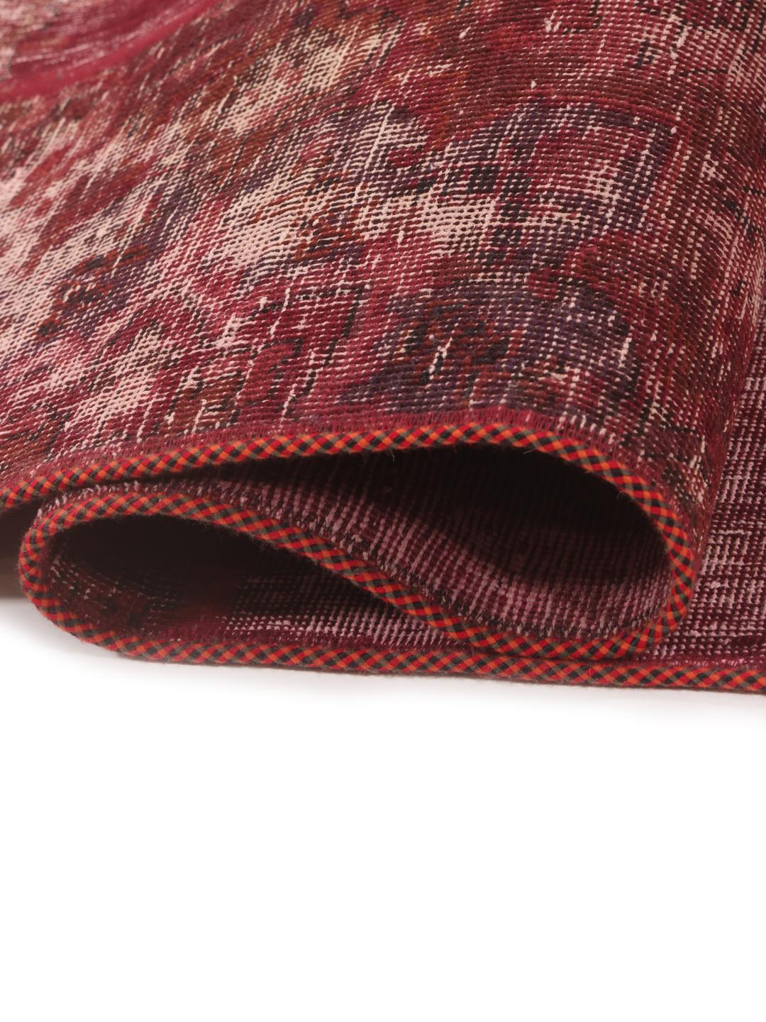 A rectangular patchwork rug with various shades of dark-red and pink tones in a hand-knotted design.