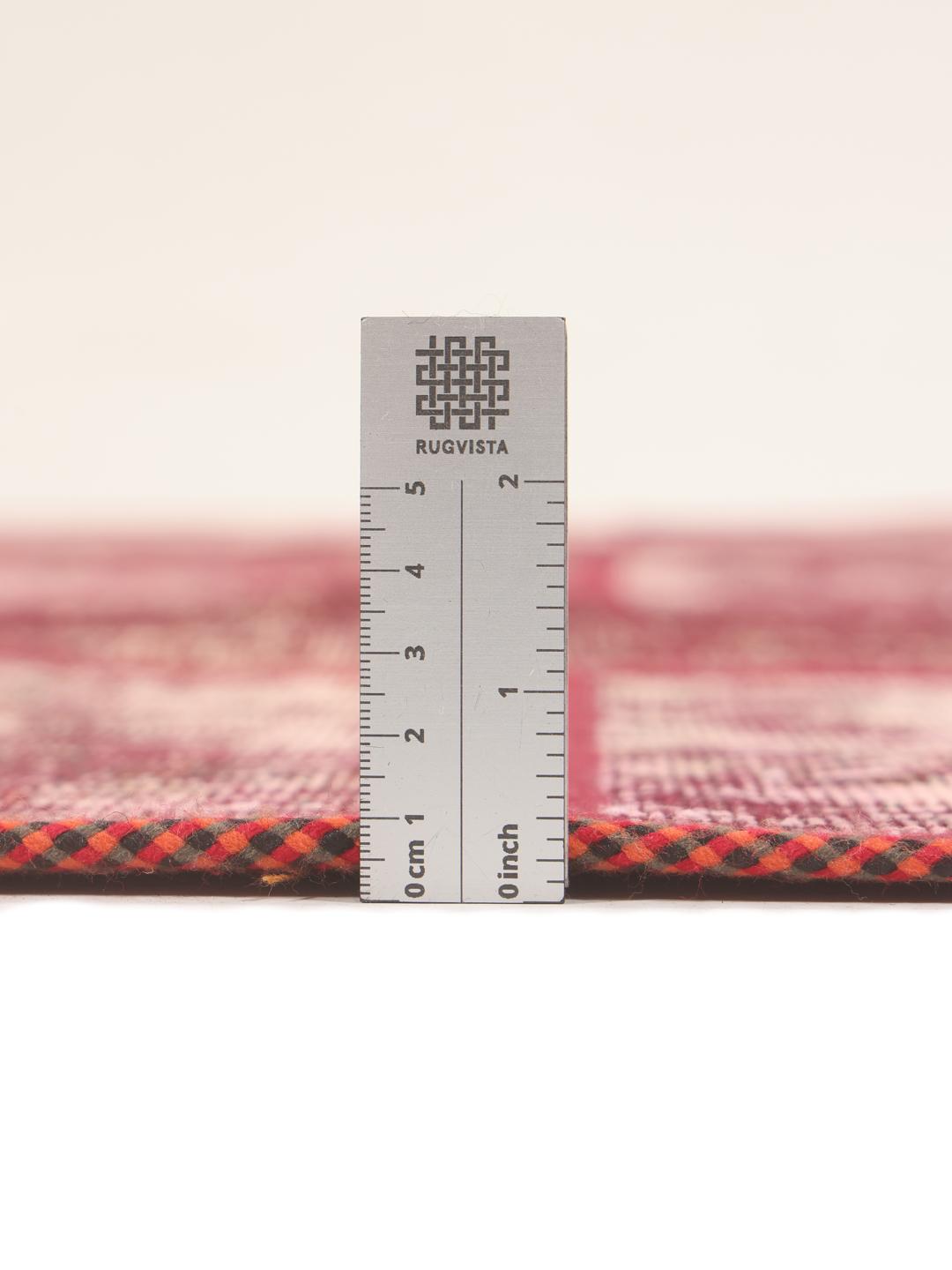 A rectangular patchwork rug with various shades of dark-red and pink tones in a hand-knotted design.
