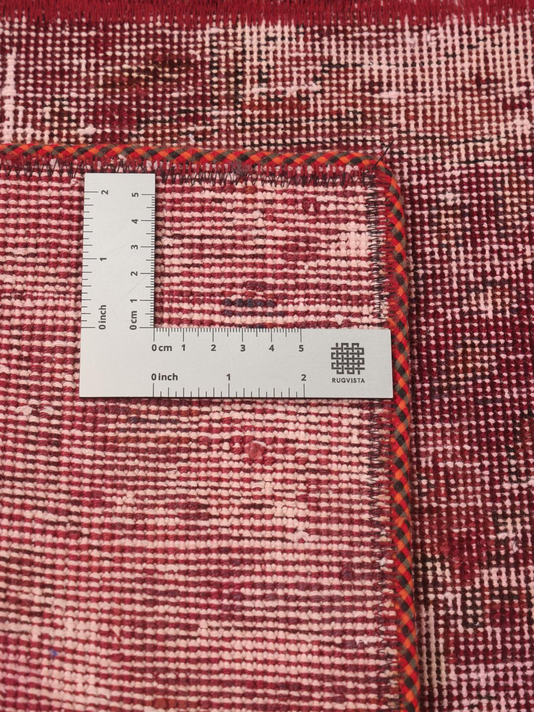 A rectangular patchwork rug with various shades of dark-red and pink tones in a hand-knotted design.