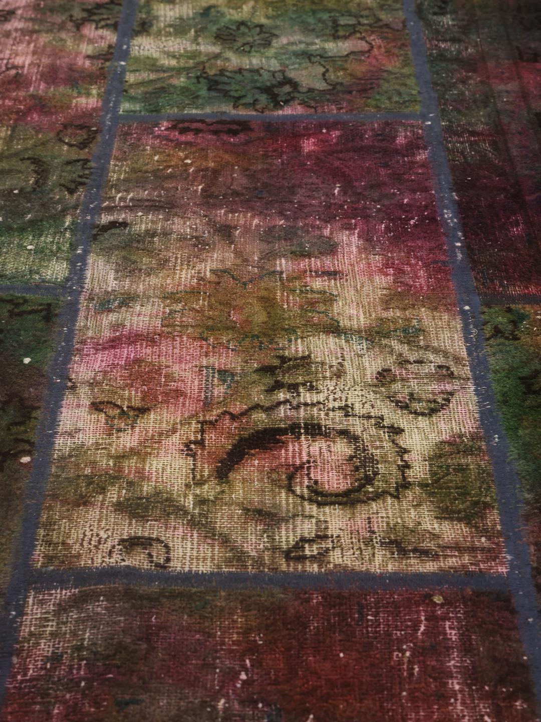 Et levende rektangulært patchwork-tæppe med forskellige tekstilmønstre fra Mellemøsten i nuancer af grøn, rød og mørke toner.