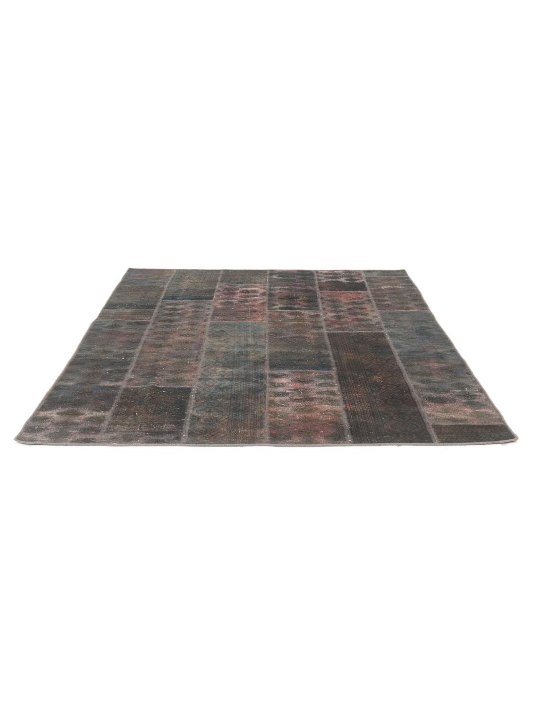A unique patchwork rug featuring various hand-knotted fragments in deep, dark-grey and red tones.