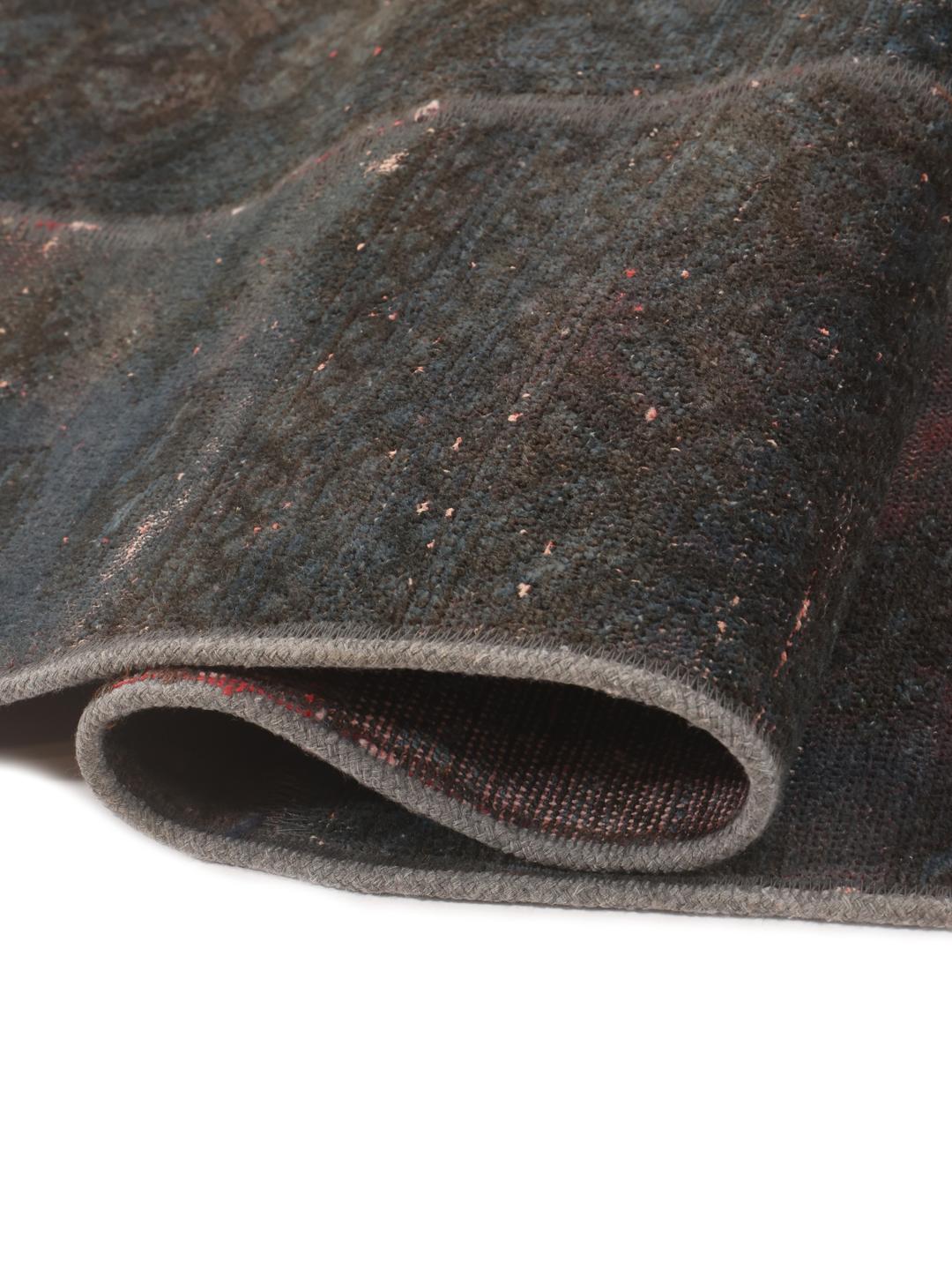 A unique patchwork rug featuring various hand-knotted fragments in deep, dark-grey and red tones.