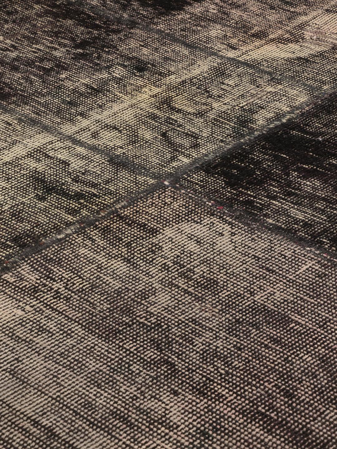Een vierkant patchwork tapijt met een donkergrijs en houtskoolkleurig kleurenschema met een verweerde, artistieke afwerking.