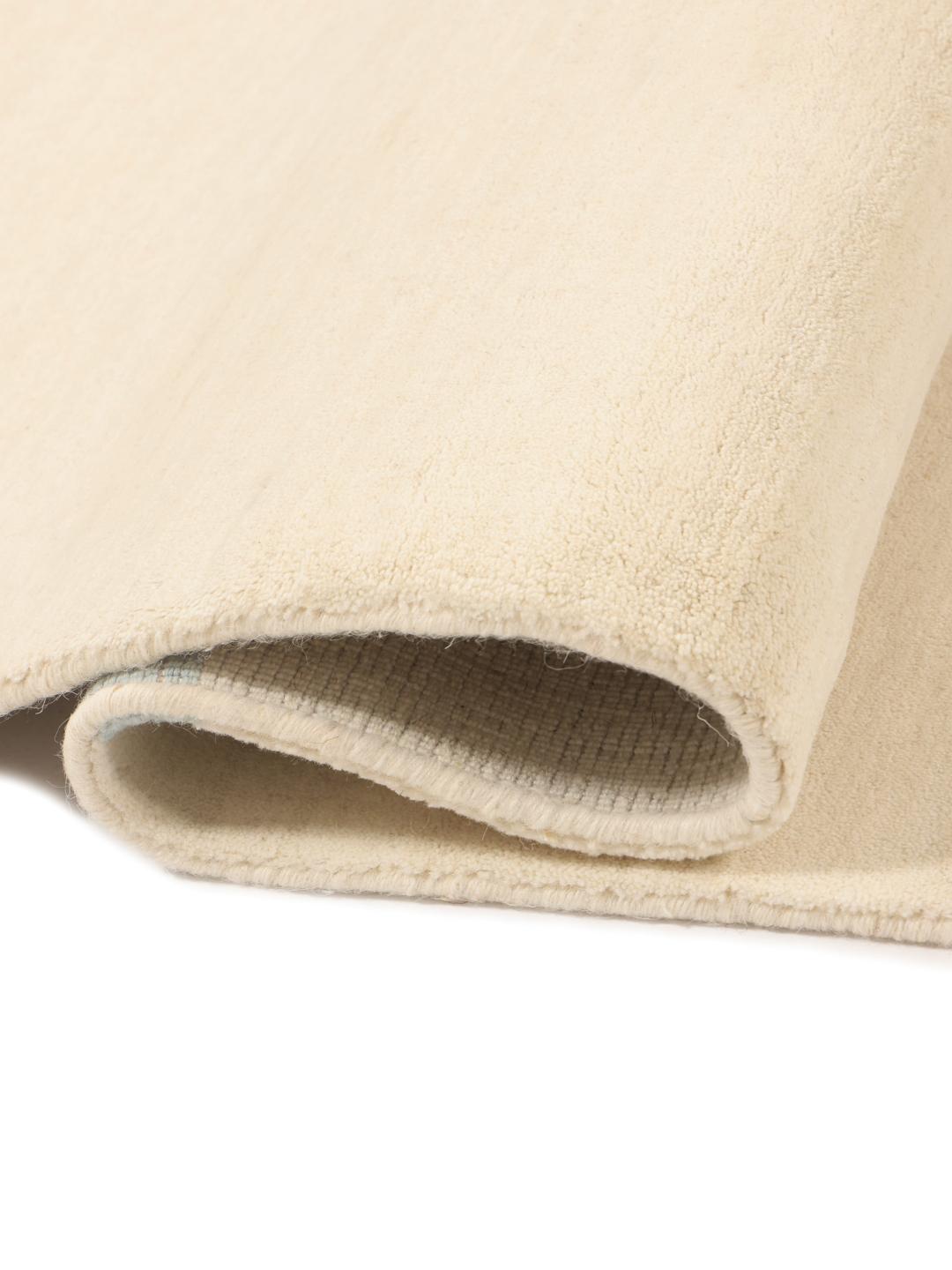 Et rektangulært håndlavet uldtæppe fra Indien med en beige base og lyseblå striber.