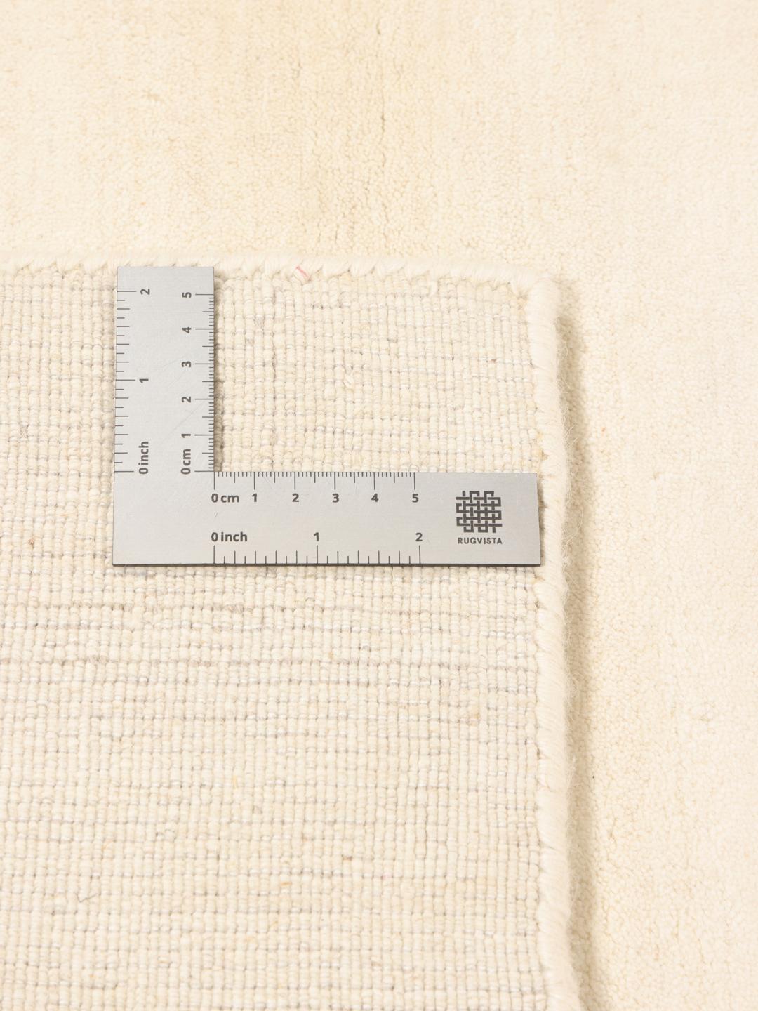 Et rektangulært håndlavet uldtæppe fra Indien med en beige base og lyseblå striber.