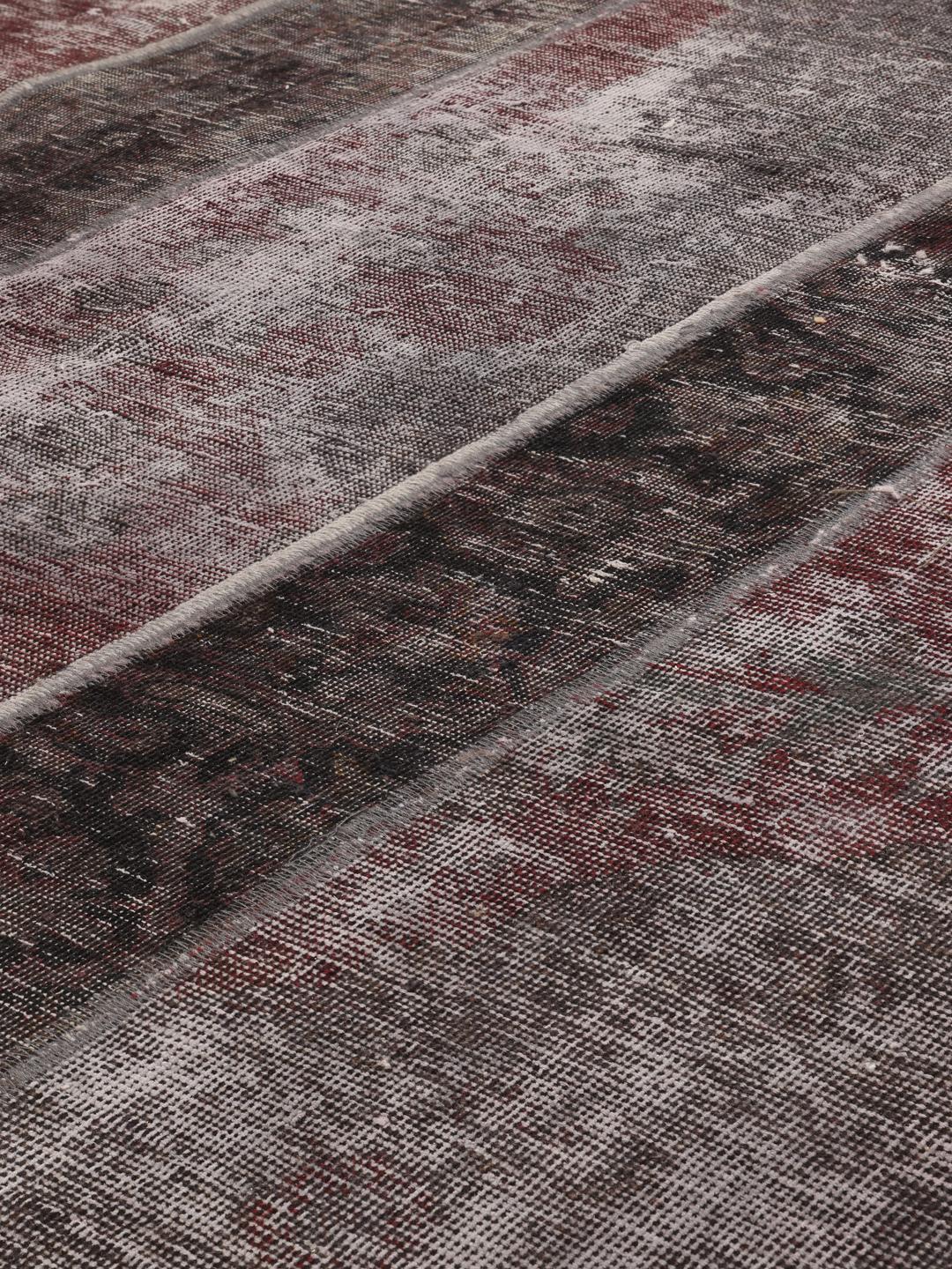 A rectangular patchwork rug featuring vertical stripes in dark-grey and deep red tones, of Middle Eastern origin.