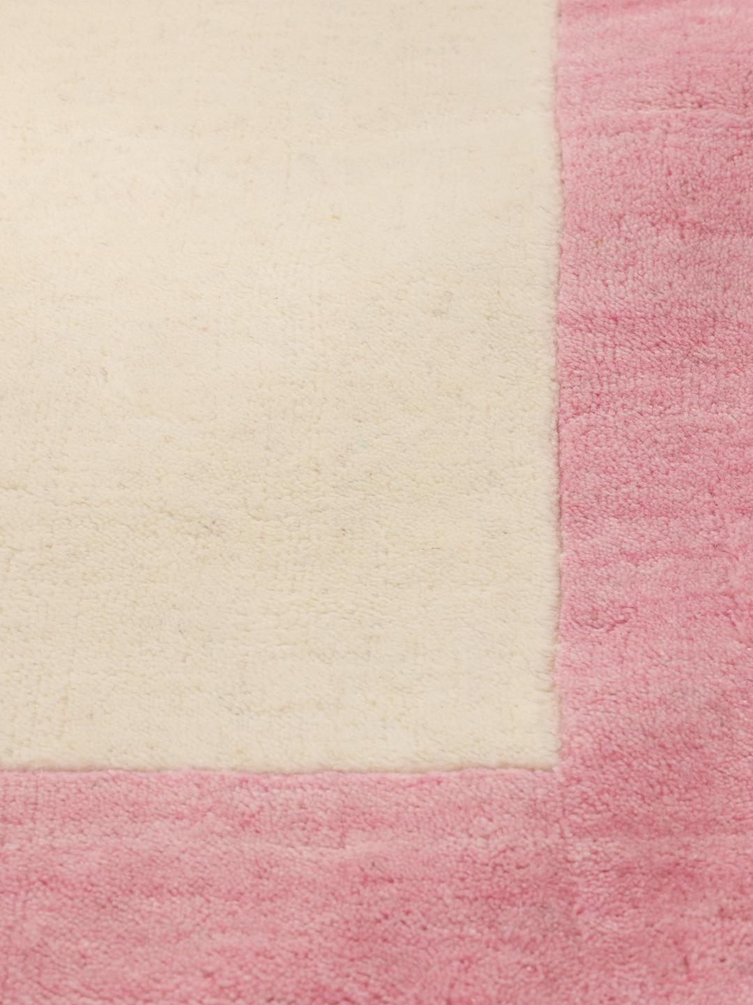 Et minimalistisk håndvævet tæppe fra Indien med beige center og pink kant