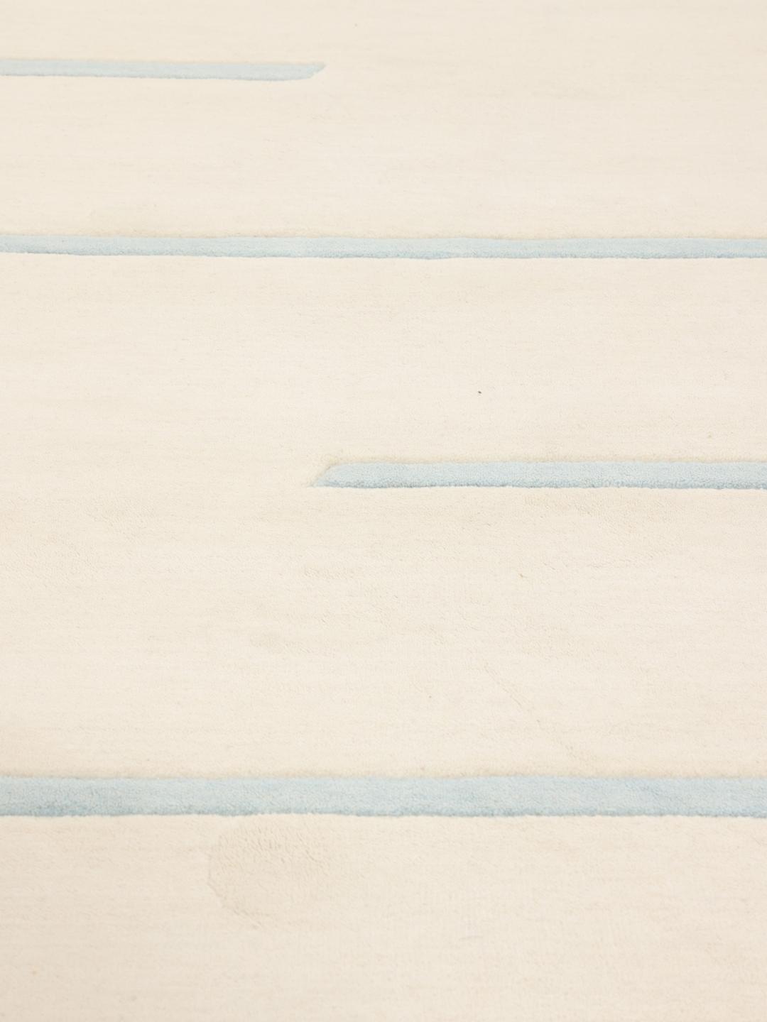 Een rond, beige handgeweven tapijt uit India met lichtblauwe horizontale strepen.