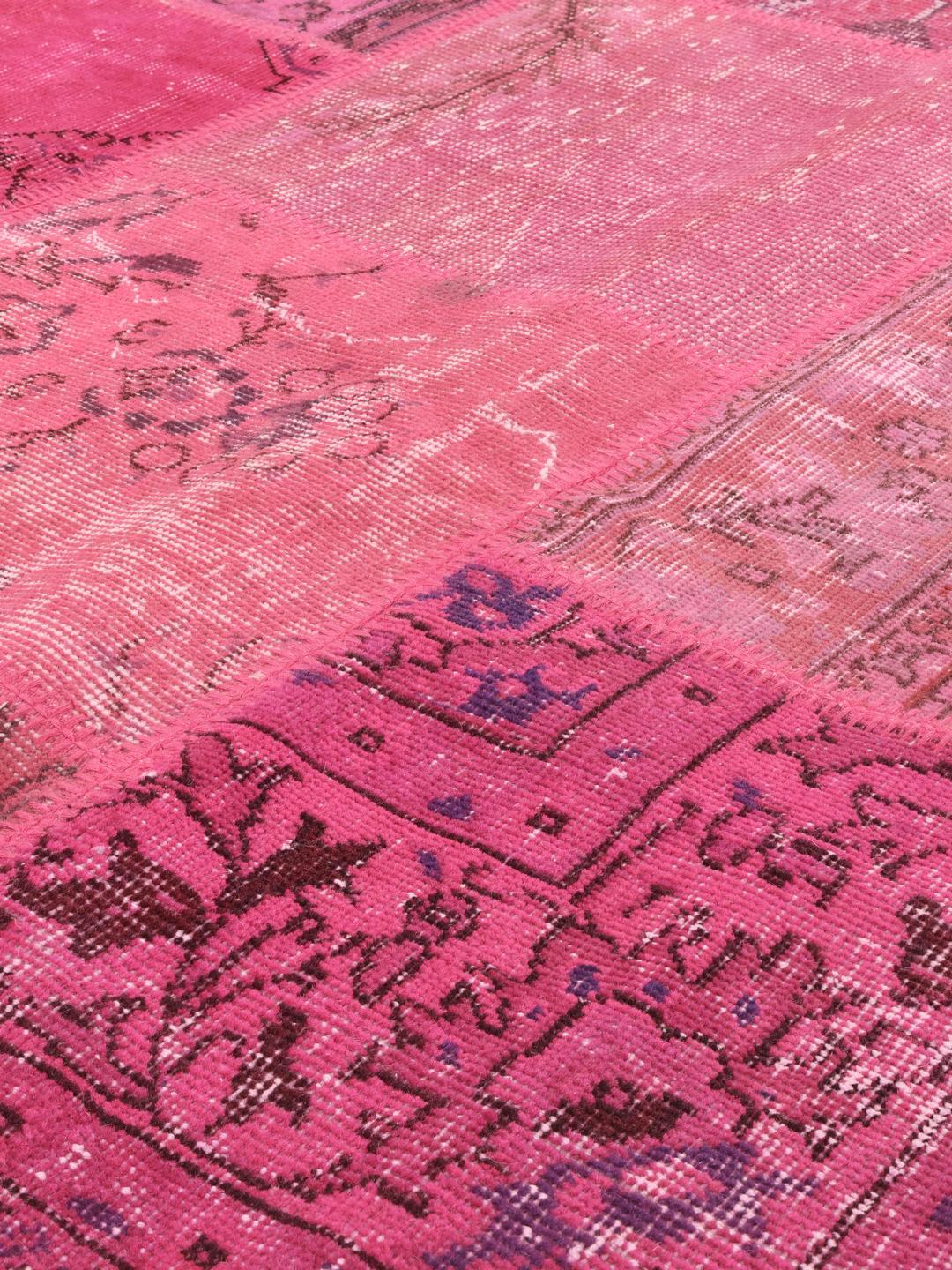 Et levende rosa tyrkisk patchwork-teppe med en rekke tradisjonelle mønstrede fragmenter.