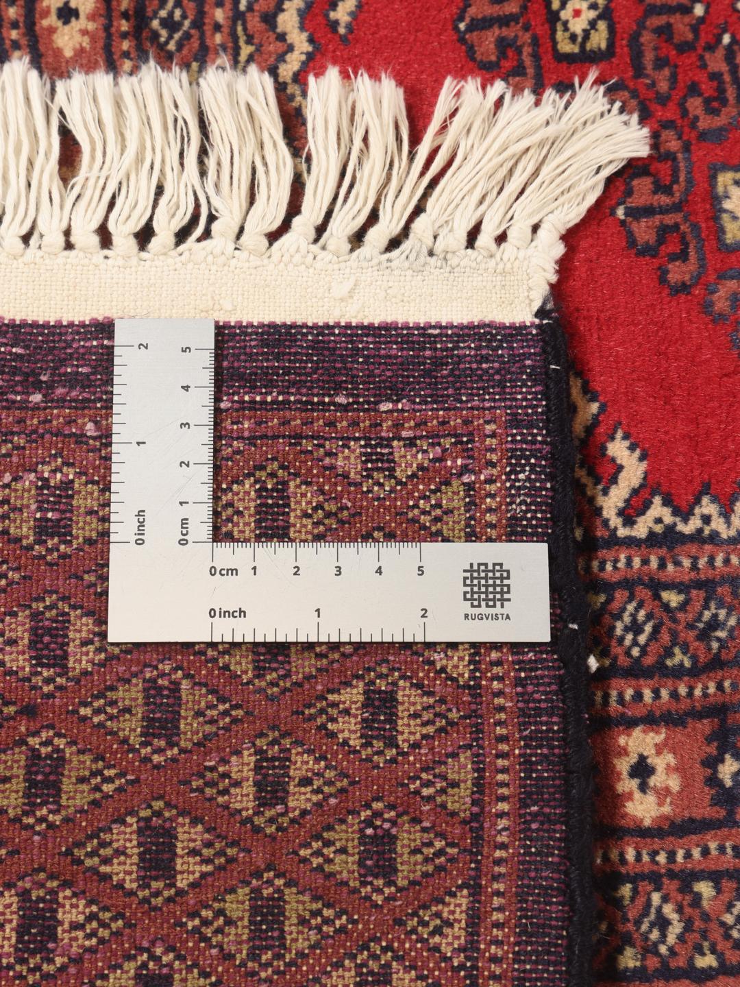 Et stort rektangulært Pakistan Bokhara tæppe med et rødt felt og gentagne geometriske motiver.