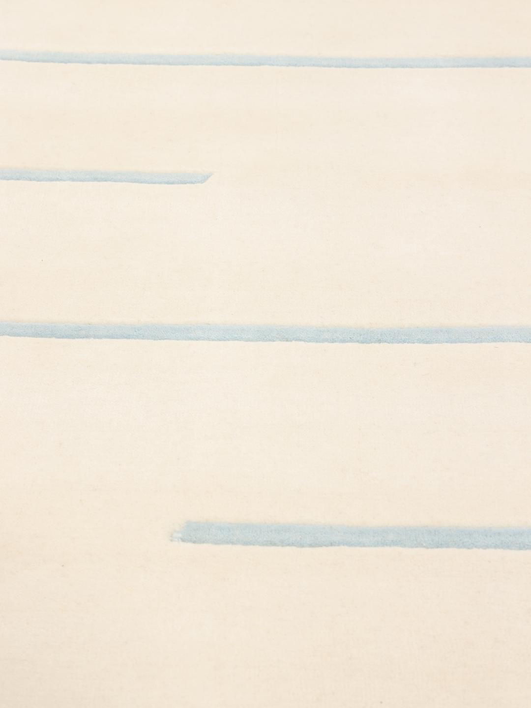 Een minimalistisch handgeweven tapijt uit India met een lichtbeige basis en subtiele blauwe gestreepte accenten.