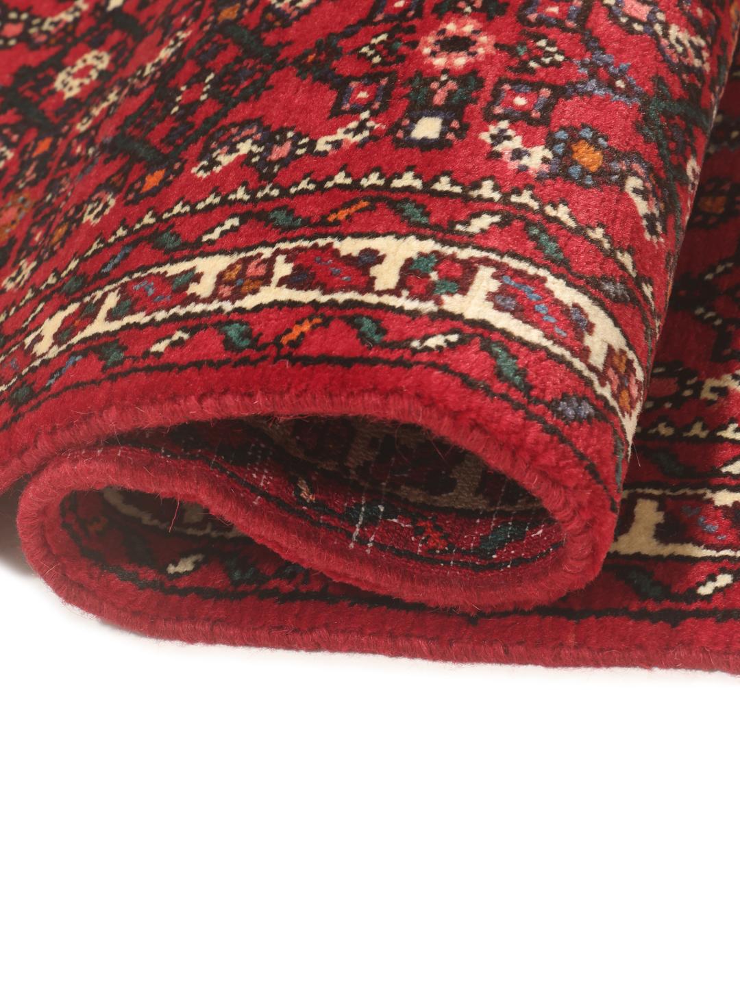 A hand-knotted Middle Eastern runner rug in deep red with intricate geometric patterns.