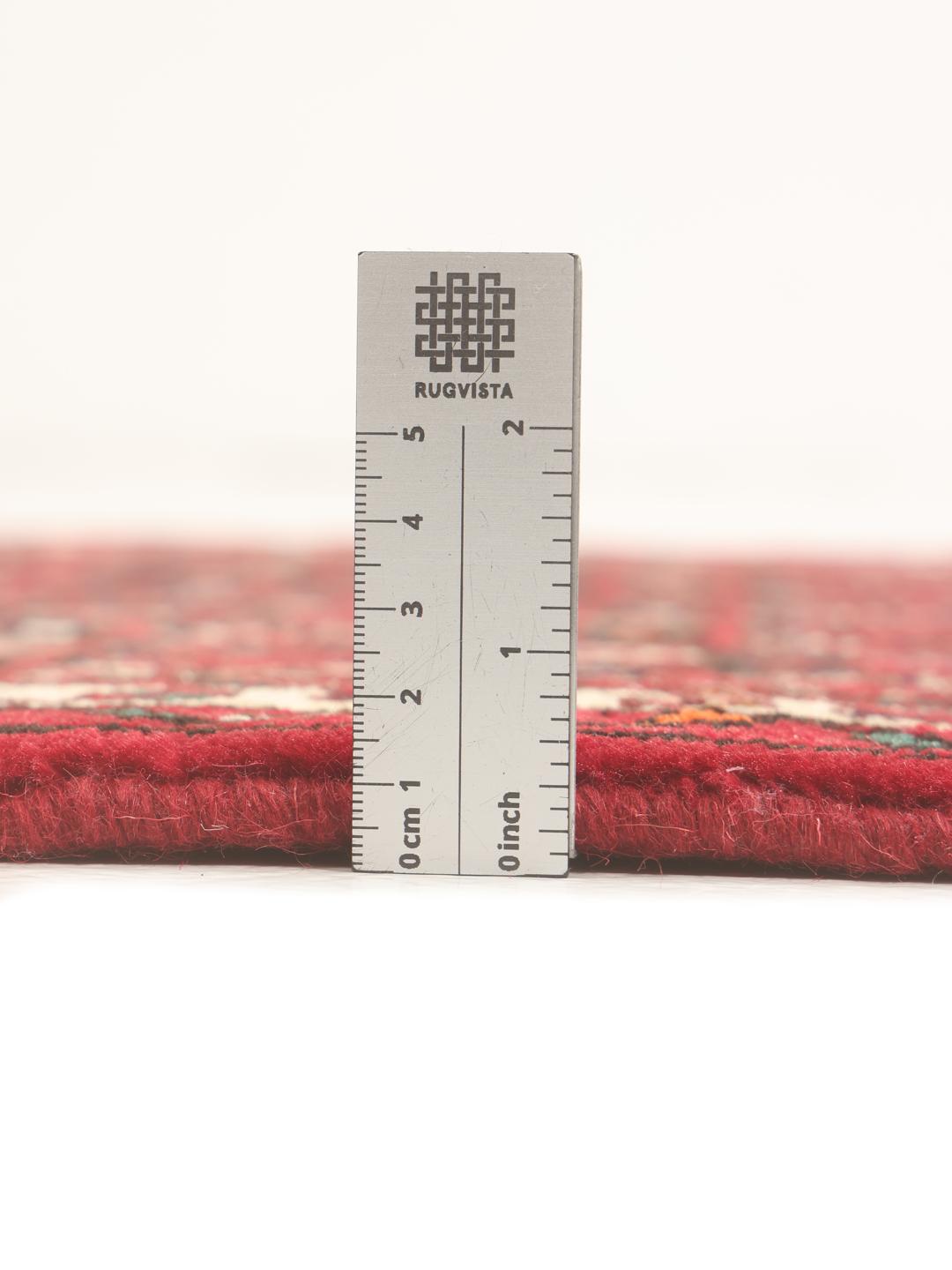 A hand-knotted Middle Eastern runner rug in deep red with intricate geometric patterns.