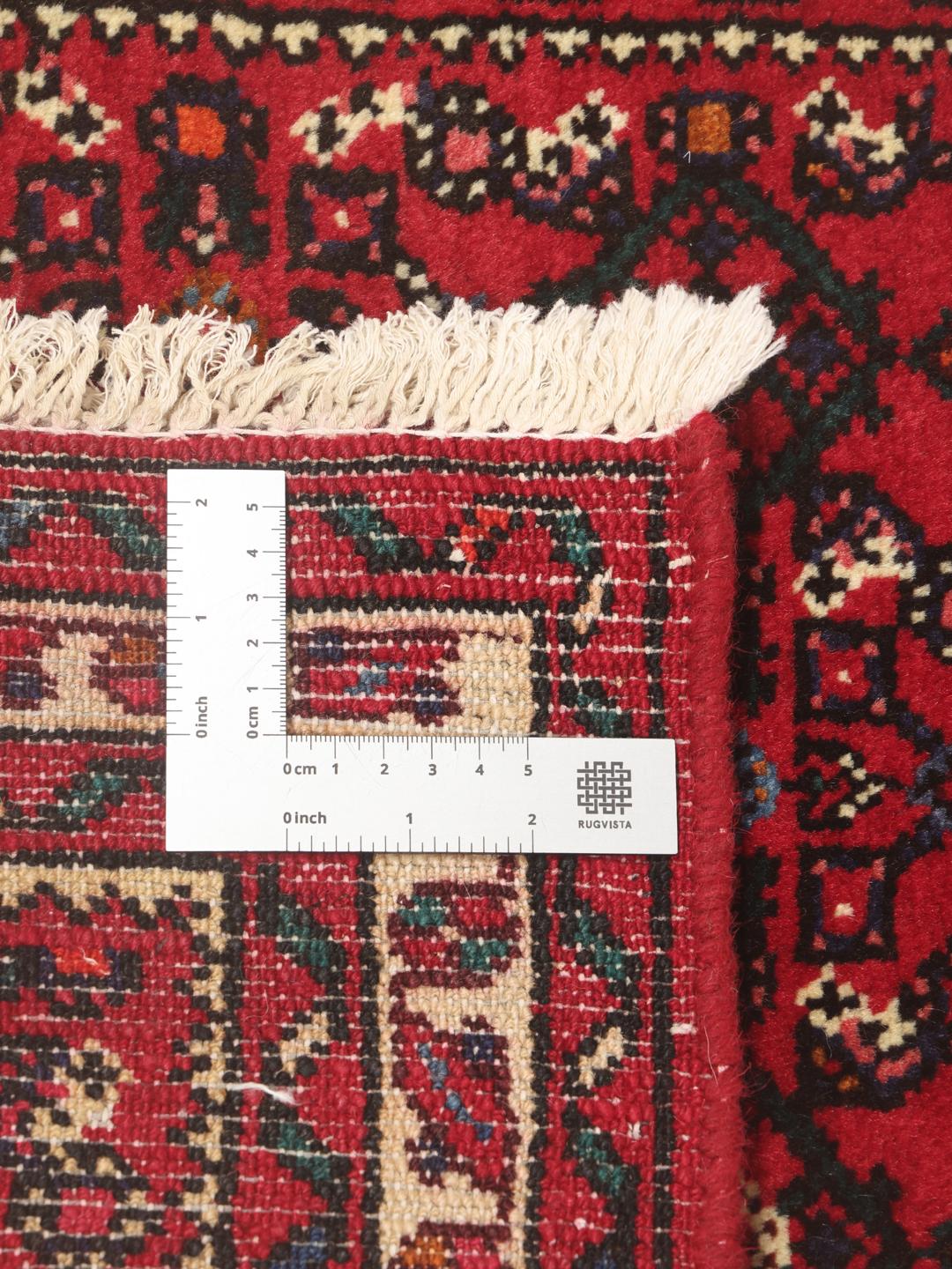 A hand-knotted Middle Eastern runner rug in deep red with intricate geometric patterns.