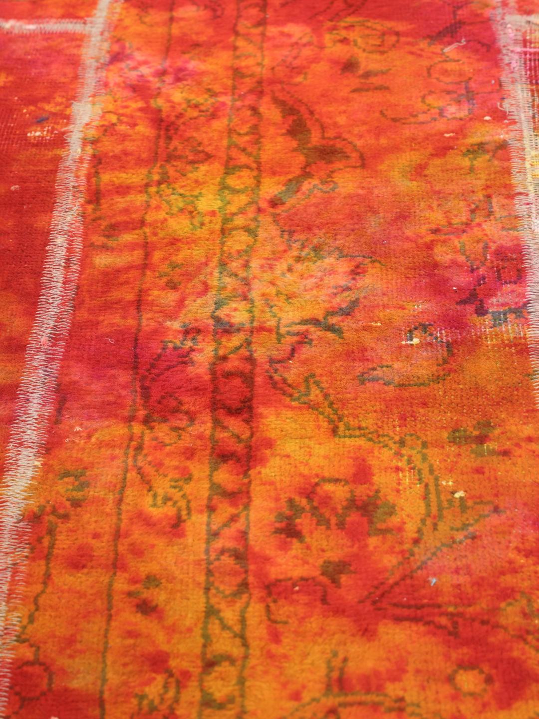 Un tapis patchwork rectangulaire vibrant provenant du Moyen-Orient, présentant un mélange de motifs floraux rouges et orange.