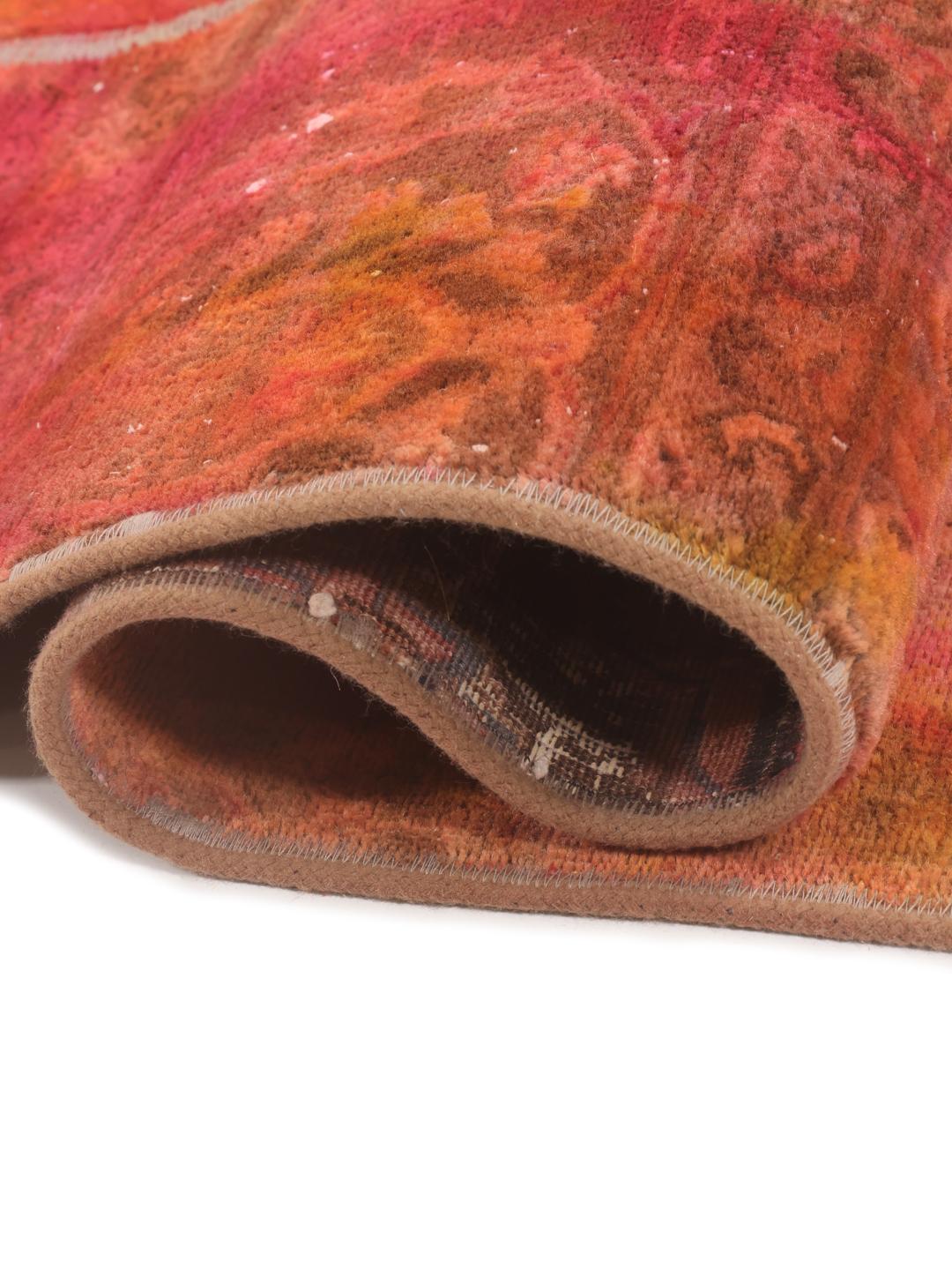A vibrant red and orange patchwork rug with intricate patterns and a textured Wool pile.