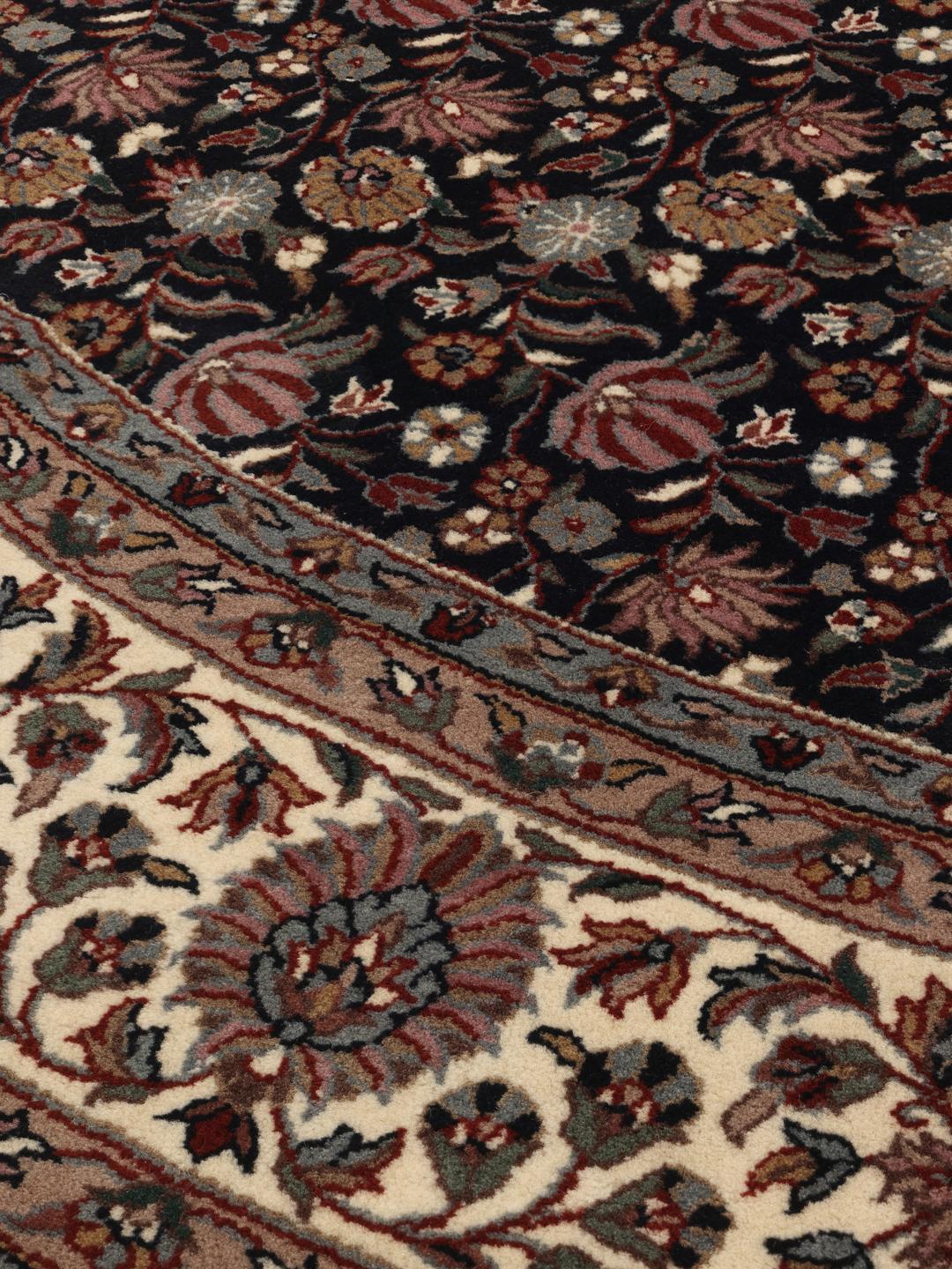 Rond handgeknoopt tapijt uit India met bloemmotieven in zwart en beige.