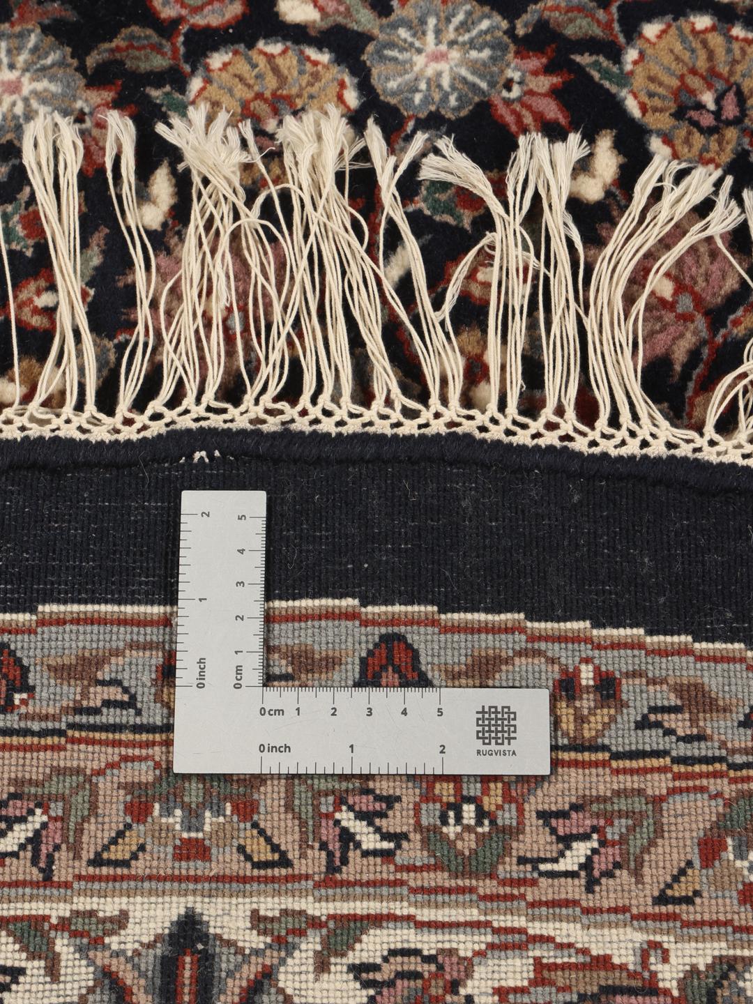 Rond handgeknoopt tapijt uit India met bloemmotieven in zwart en beige.
