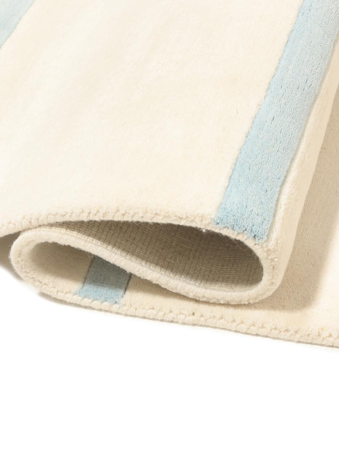 Een groot rechthoekig handgeweven tapijt uit India met een minimalistisch gestreept patroon in beige en blauw.