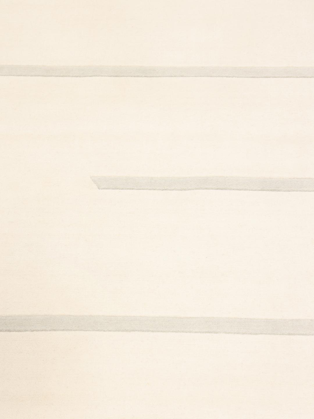 Et moderne, håndvævet tæppe fra Indien i en blød beige farve med minimalistiske stribede mønstre.