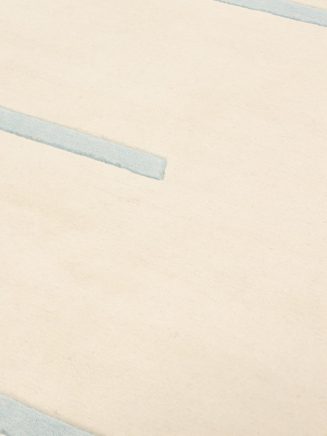Et stort rektangulært håndvævet tæppe fra Indien med en beige baggrund og et lyseblåt horisontalt stribemønster.