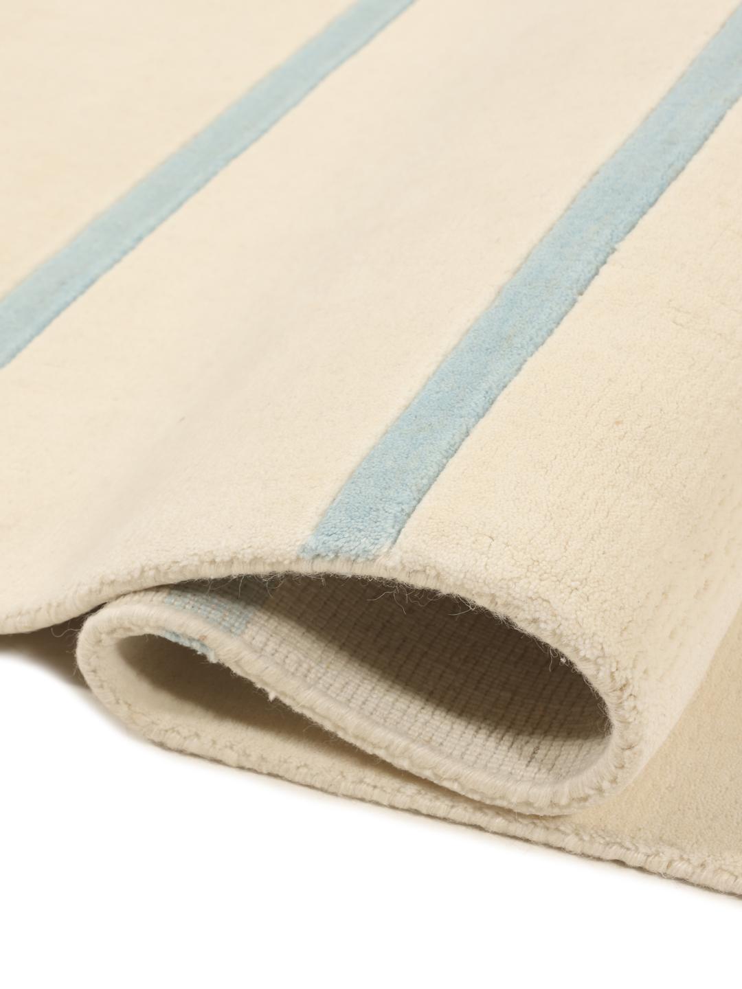 Et stort rektangulært håndvævet tæppe fra Indien med en beige baggrund og et lyseblåt horisontalt stribemønster.