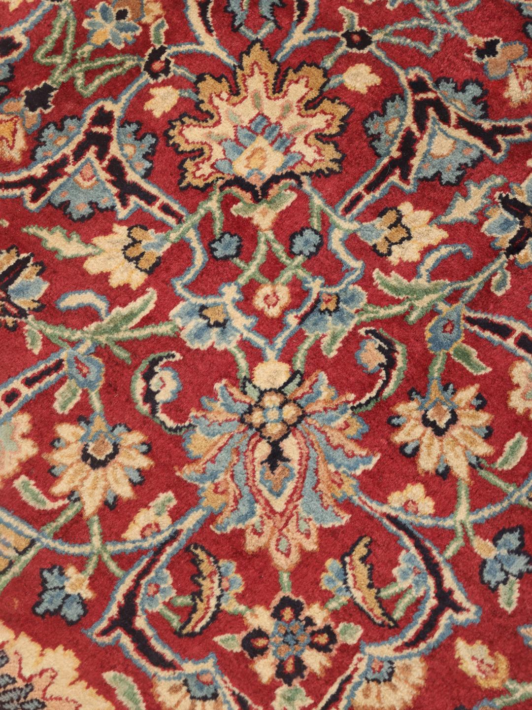 Een groot Kerman-tapijt uit het Midden-Oosten met een rood bloemmotief en een donkerblauwe rand.