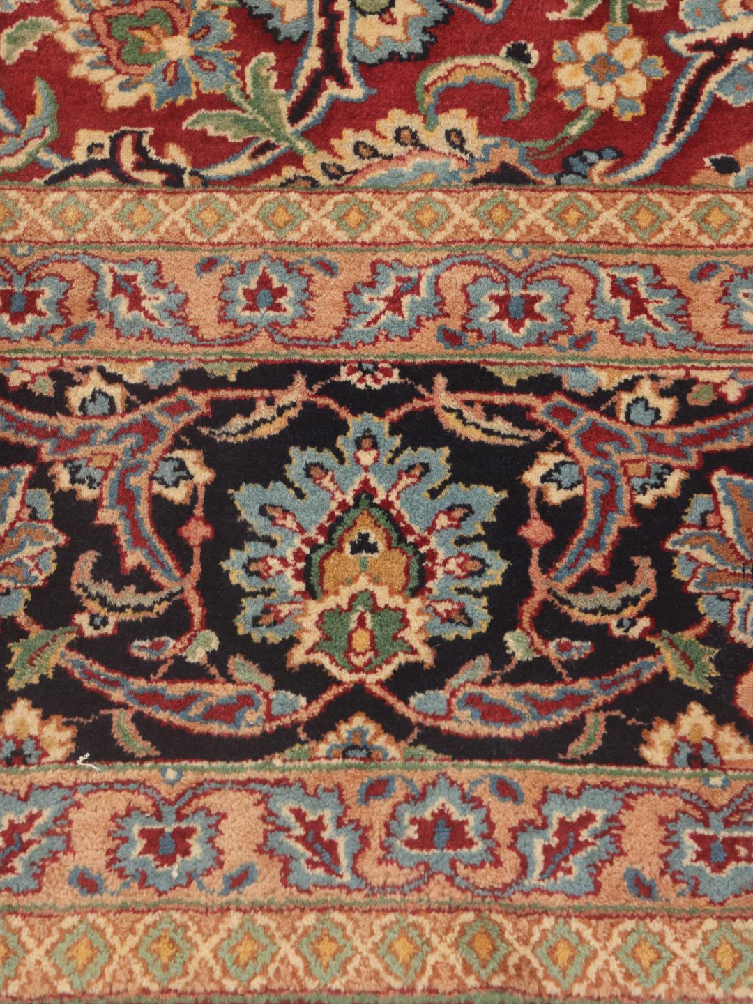 Een groot Kerman-tapijt uit het Midden-Oosten met een rood bloemmotief en een donkerblauwe rand.