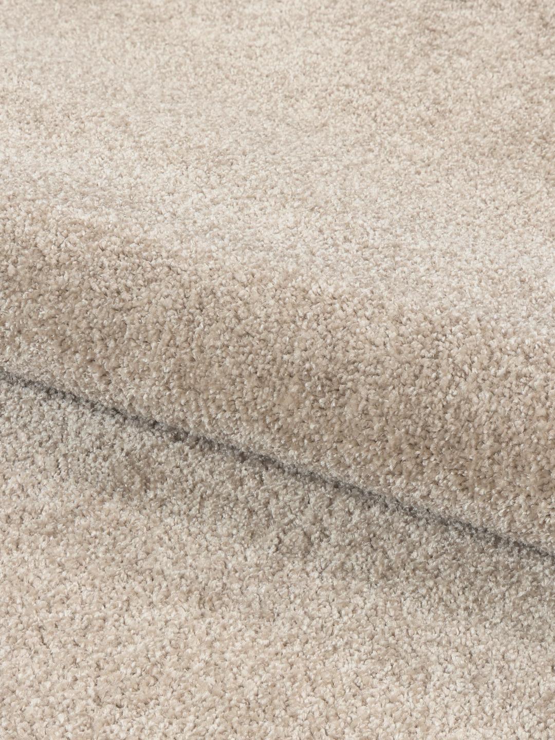 Beige tapijt met een onregelmatige vorm en zachte pooltextuur.