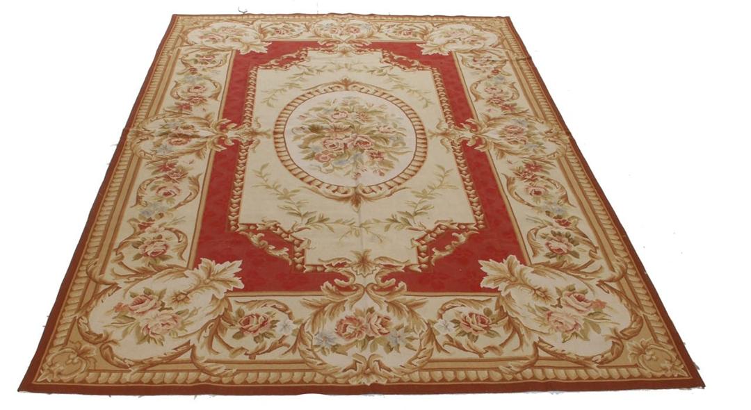 Et rektangulært, håndvævet tæppe fra Kina med et rødt og beige blomstermedaillon-design.