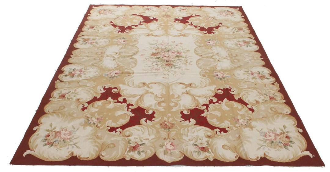 Et rektangulært, håndvævet tæppe fra Kina med et rødt og beige blomstermedaillon-design.