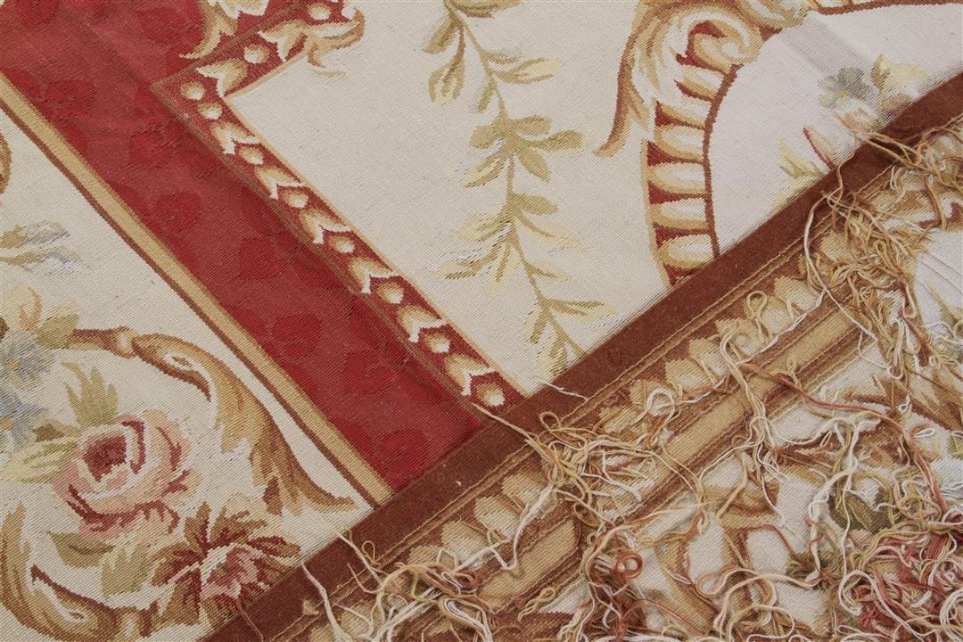 Et rektangulært, håndvævet tæppe fra Kina med et rødt og beige blomstermedaillon-design.