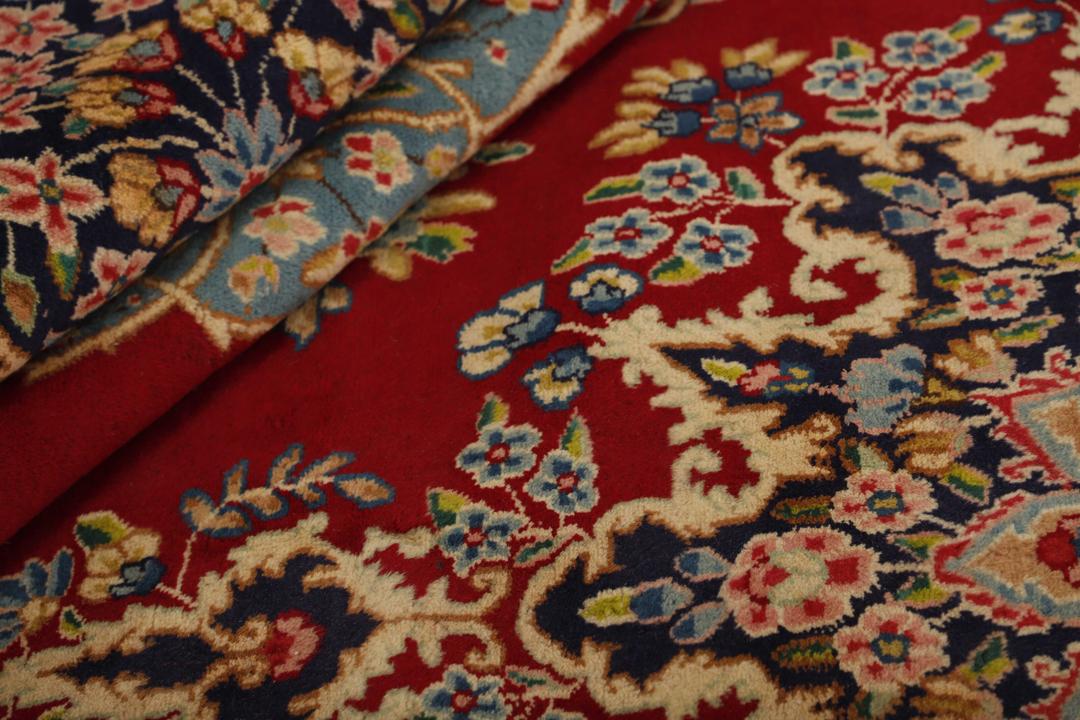 Een handgeknoopt Kerman-tapijt uit het Midden-Oosten met een rood veld en ingewikkelde bloemmotieven