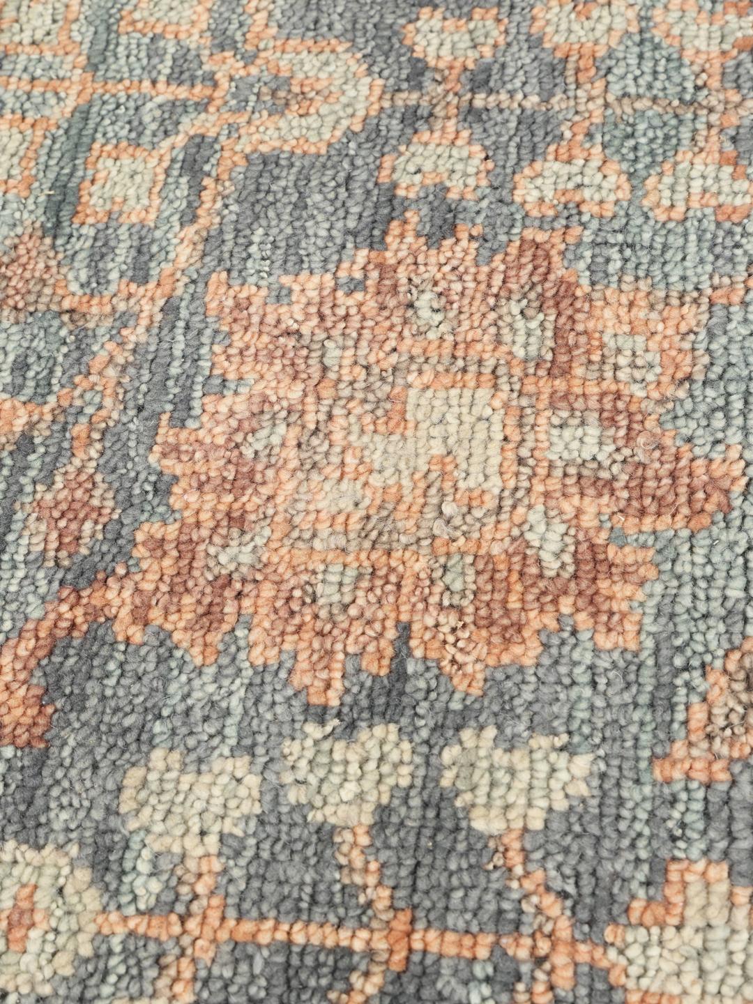 Una alfombra redonda de lana Usak Indo con diseño floral en tonos grises y apagados de la India