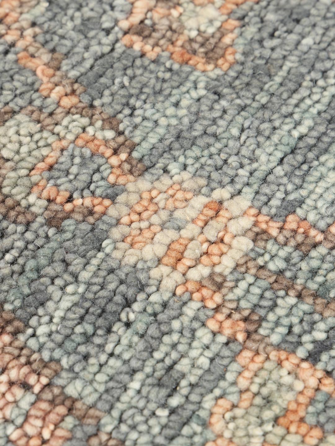 Una alfombra redonda de lana Usak Indo con diseño floral en tonos grises y apagados de la India