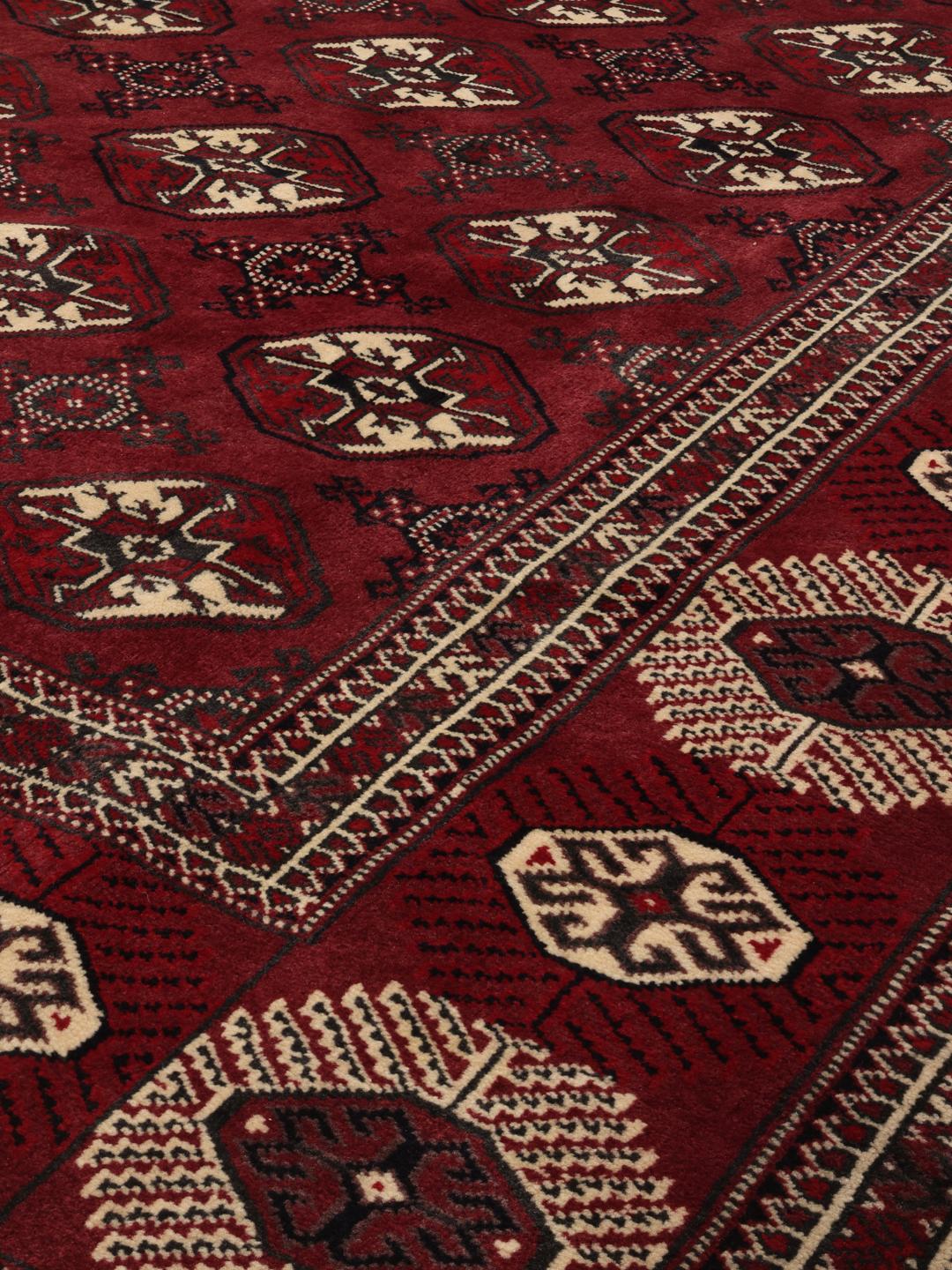 A hand-knotted Middle Eastern Turkman rug featuring deep red tones and geometric patterns.
