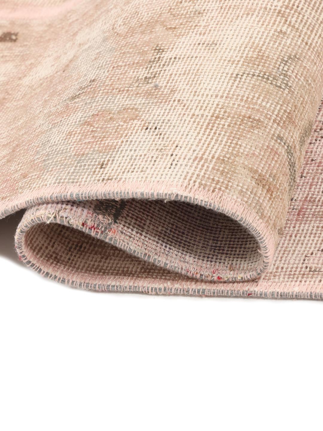 Een vierkant patchwork tapijt met zachte roze en beige tinten en vervaagde motieven uit het Midden-Oosten.