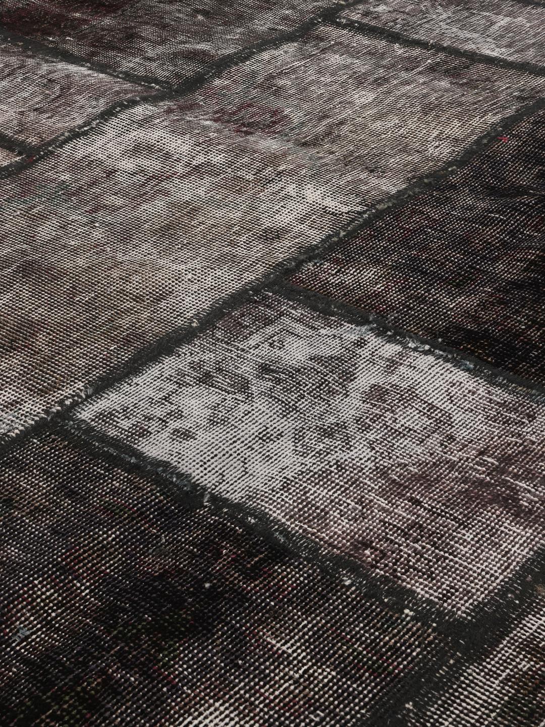 Et rundt patchwork-tæppe i en mørkegrå og koksgrå farvepalette med varierede geometriske teksturer.