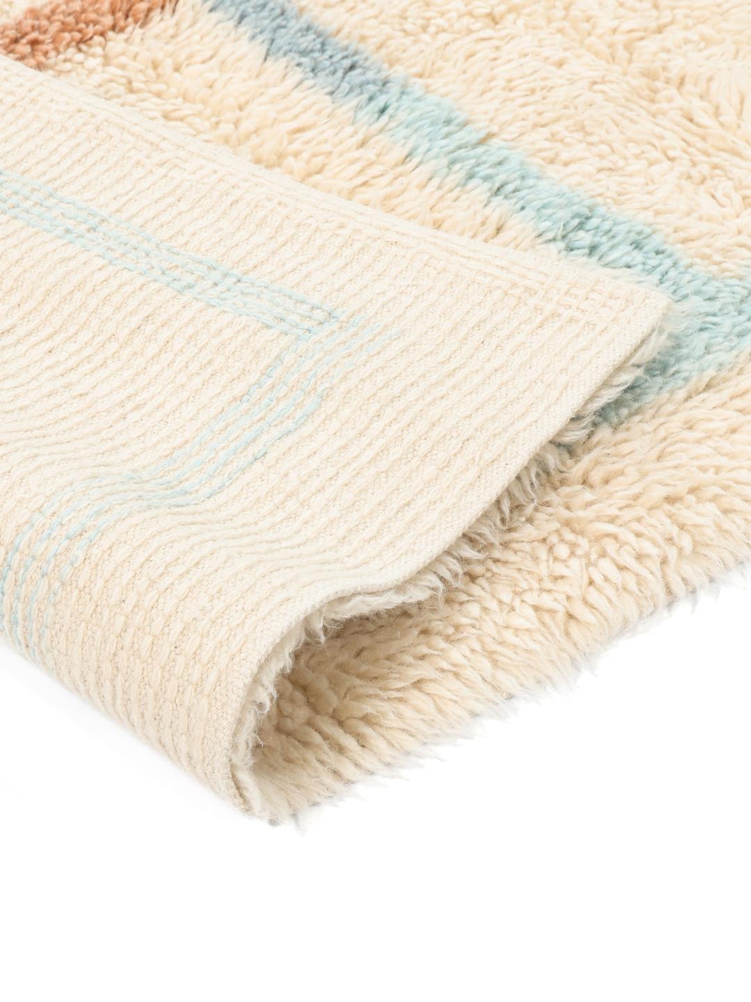 Beige tæppe med blød luv og et diskret flerfarvet ternet design