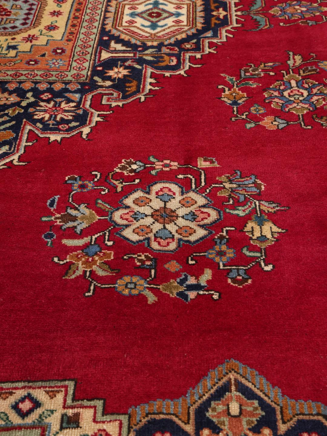 Een handgeknoopt Tabriz-tapijt uit het Midden-Oosten met een levendig rood veld en een centraal medaillon.