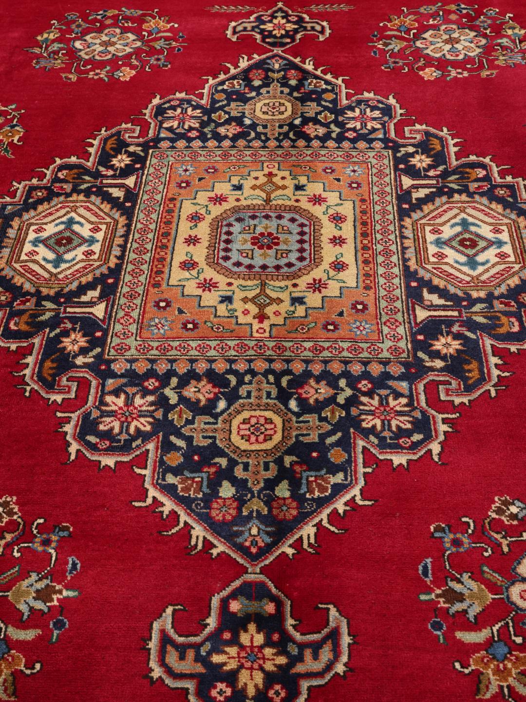 Een handgeknoopt Tabriz-tapijt uit het Midden-Oosten met een levendig rood veld en een centraal medaillon.