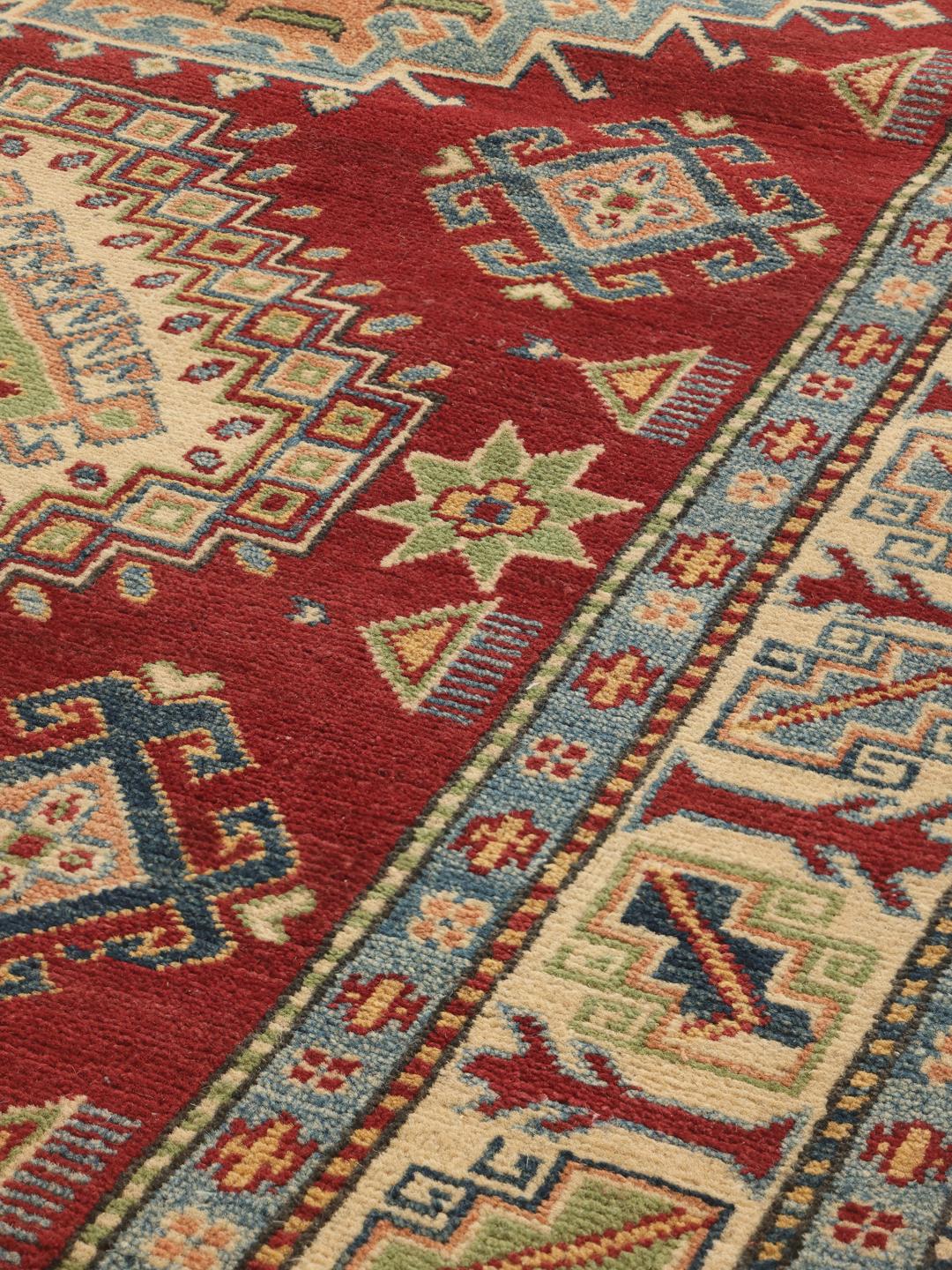 Een handgeknoopt Kazak-tapijt uit Afghanistan met een rood veld en geometrische medaillons.