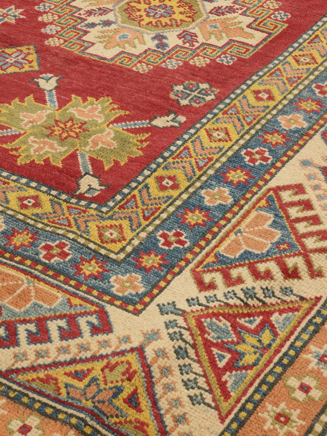 Un covor Kazak înnodat manual din Afganistan, având un câmp roșu vibrant și modele geometrice de medalion.