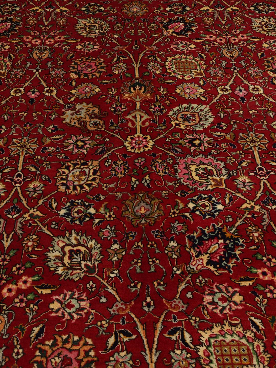 A large rectangular Tabriz rug with a deep red field and intricate floral patterns.