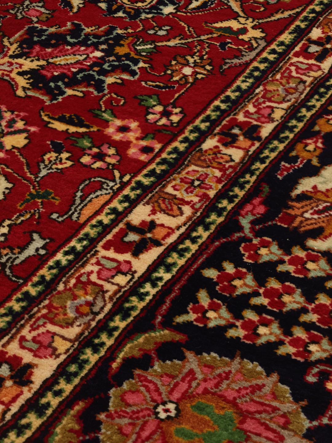 A large rectangular Tabriz rug with a deep red field and intricate floral patterns.