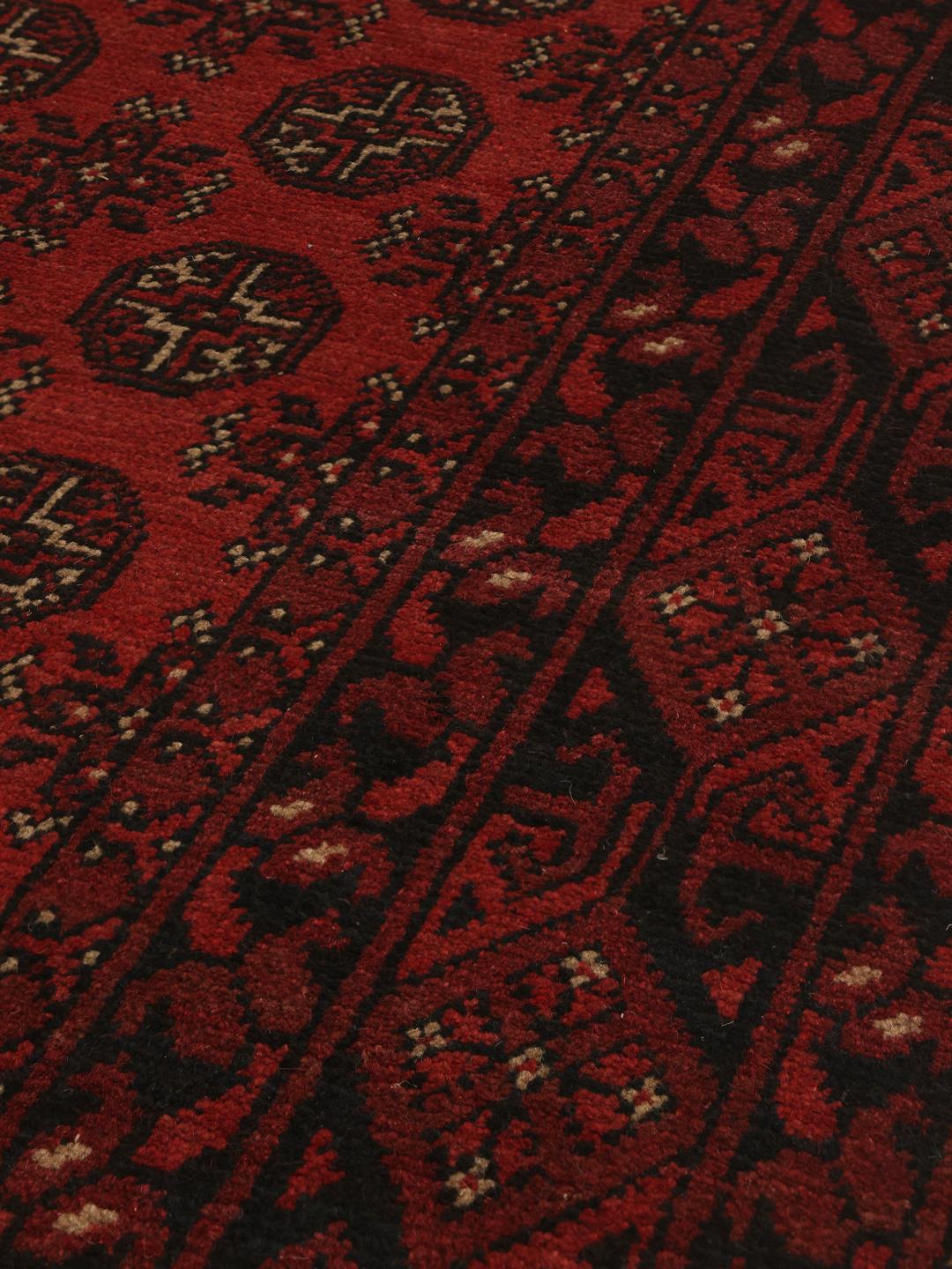 Håndknyttet afghansk tæppe med en dyb rød bund og geometriske motiver
