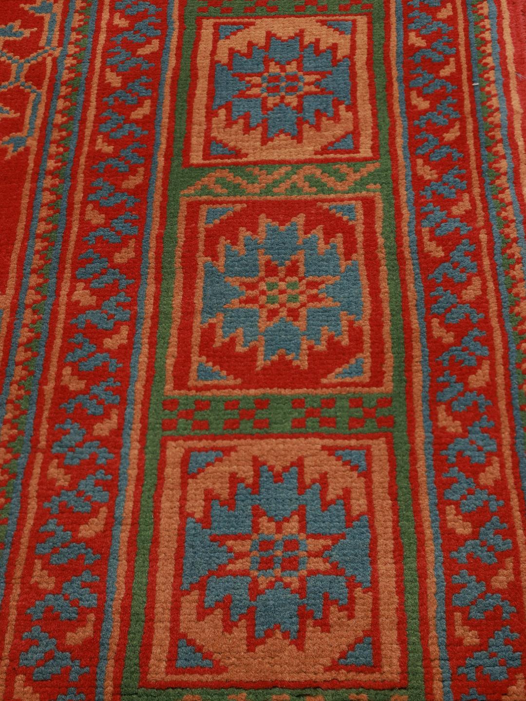 Håndknyttet afghansk tæppe med rød bund og traditionelle geometriske motiver