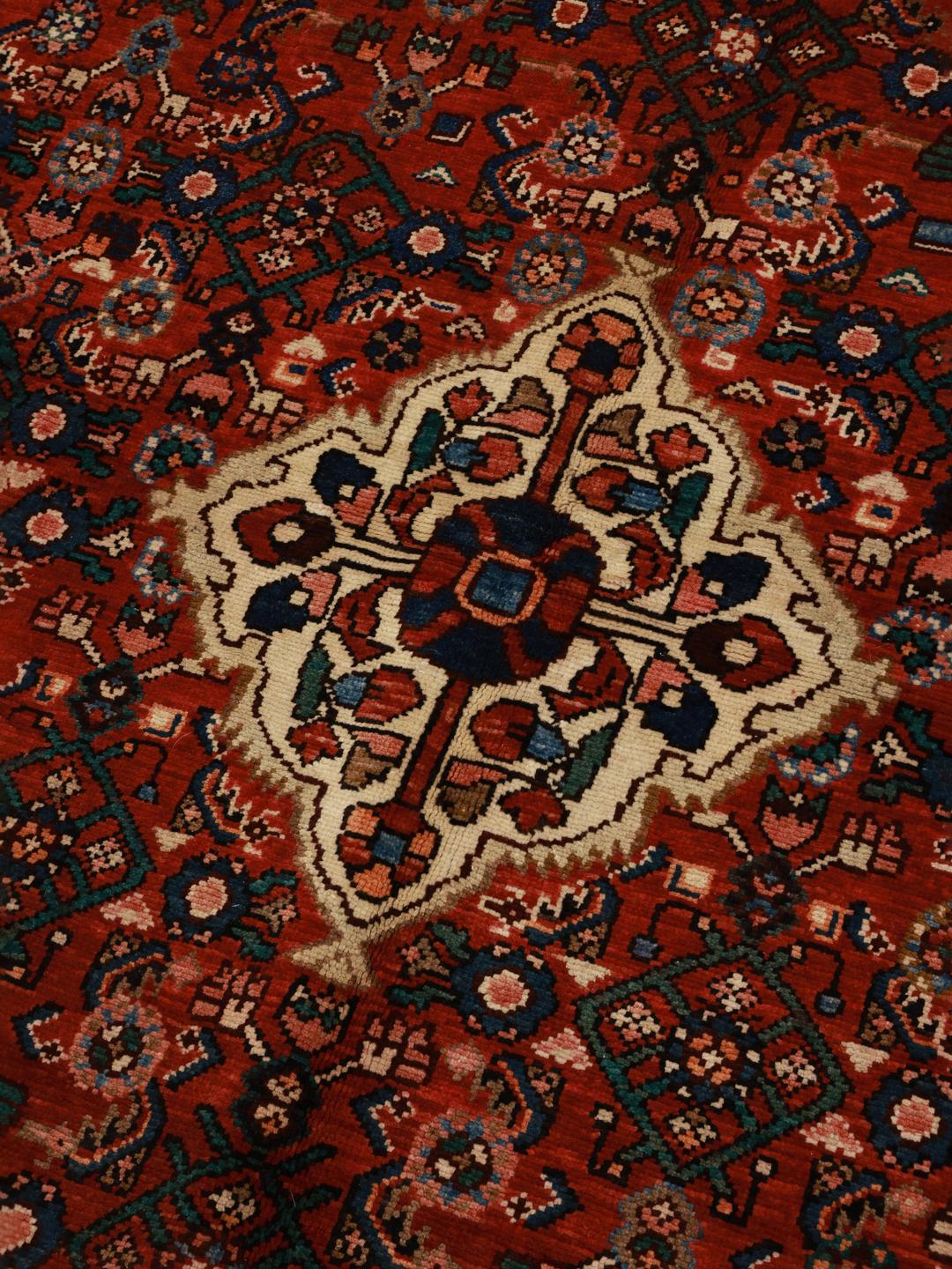 Et håndknyttet Hosseinabad-tæppe fra Mellemøsten med et rødt felt og traditionelle motiver.